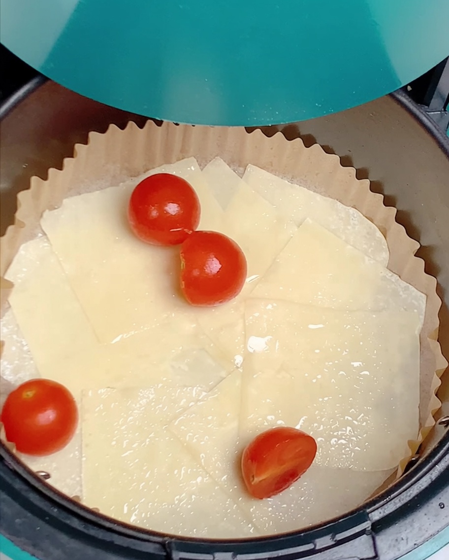 Mitades de tomates cherry esparcidas sobre láminas de wonton en la freidora.