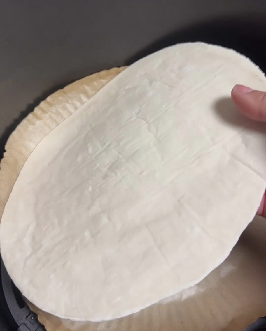Una tortita de cebolleta cruda plana en la cesta de una freidora de aire forrada con papel pergamino.