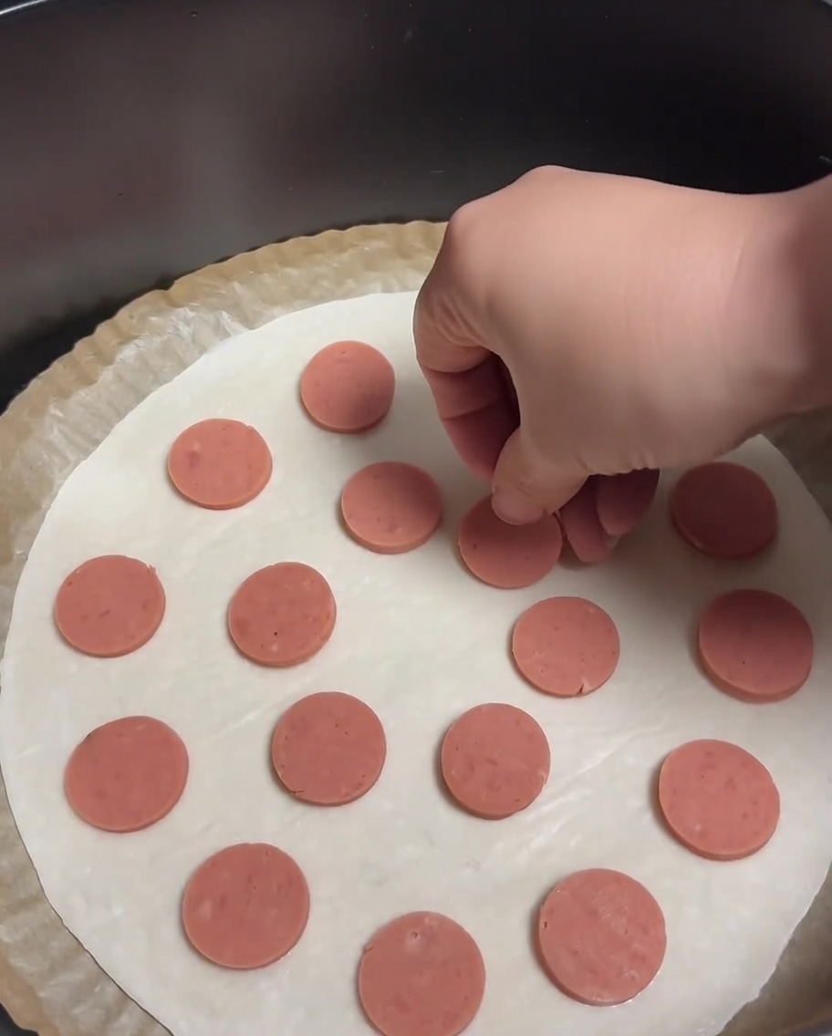 Una tortita de cebolleta cubierta con rodajas circulares de salchicha distribuidas uniformemente.
