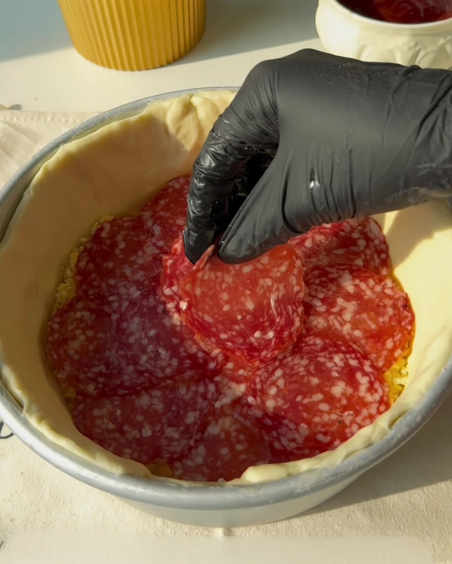 Tiras de tocino poniéndose sobre la capa de salami.
