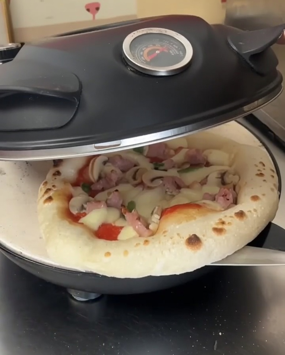 Una pizza parcialmente cocinada con el queso derretido dentro de un horno abierto, siendo rotada con una pala de metal.