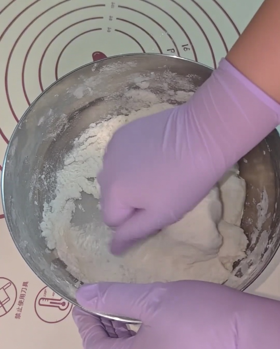 Manos con guantes morados amasando la masa dentro de un bol de metal.