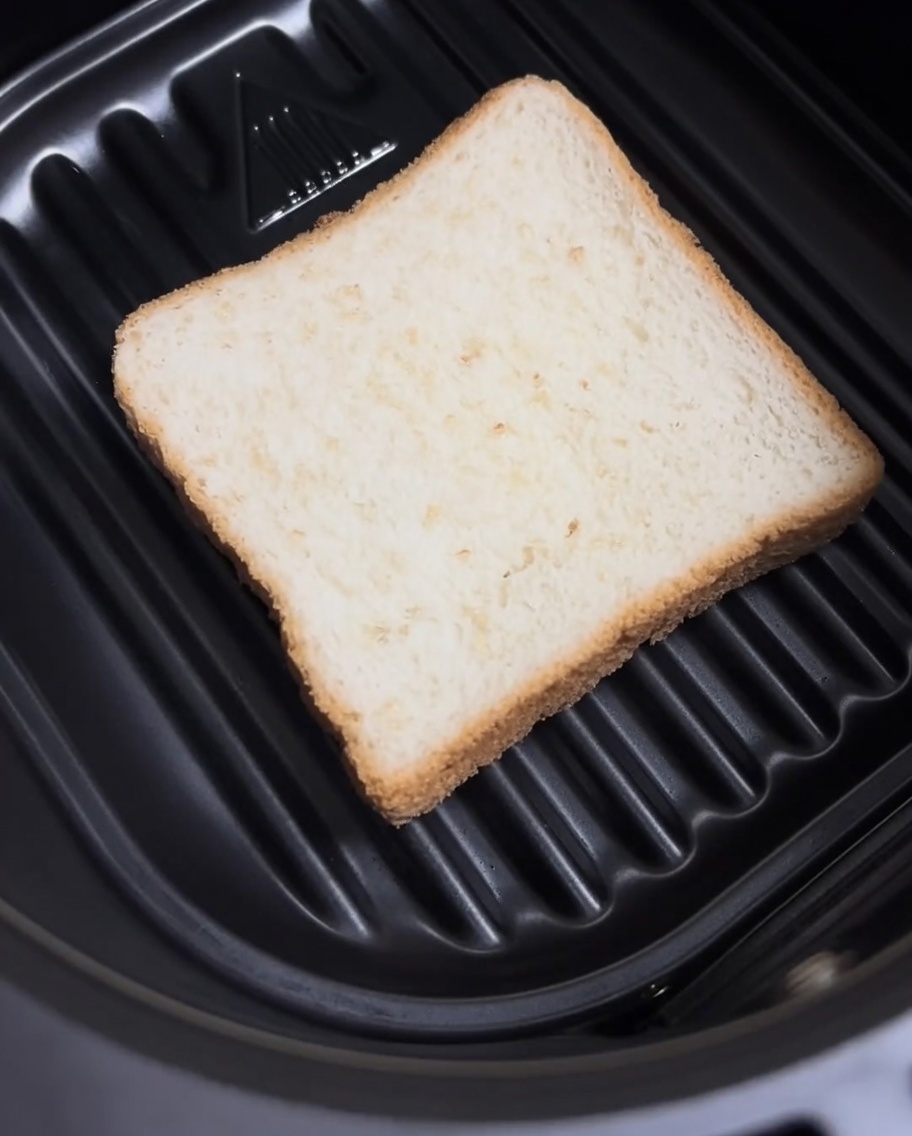 Una rebanada de pan blanco colocada plana en la base de la canasta de la air fryer.