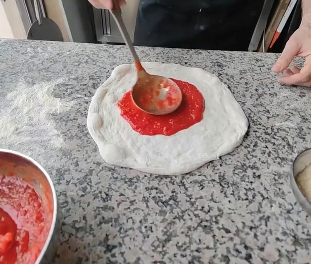 Extendiendo salsa de tomate roja en el centro de la masa estirada con un cucharón.