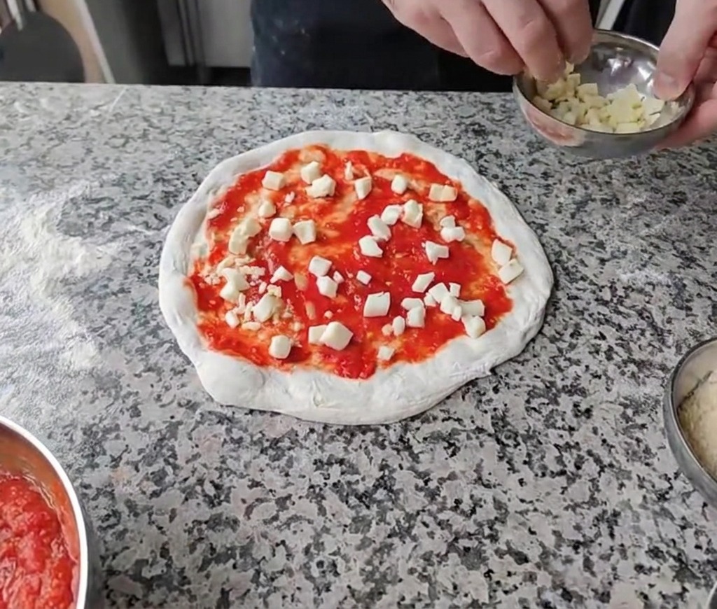 Esparciendo quesos blancos en dados uniformemente sobre la base de salsa de tomate.