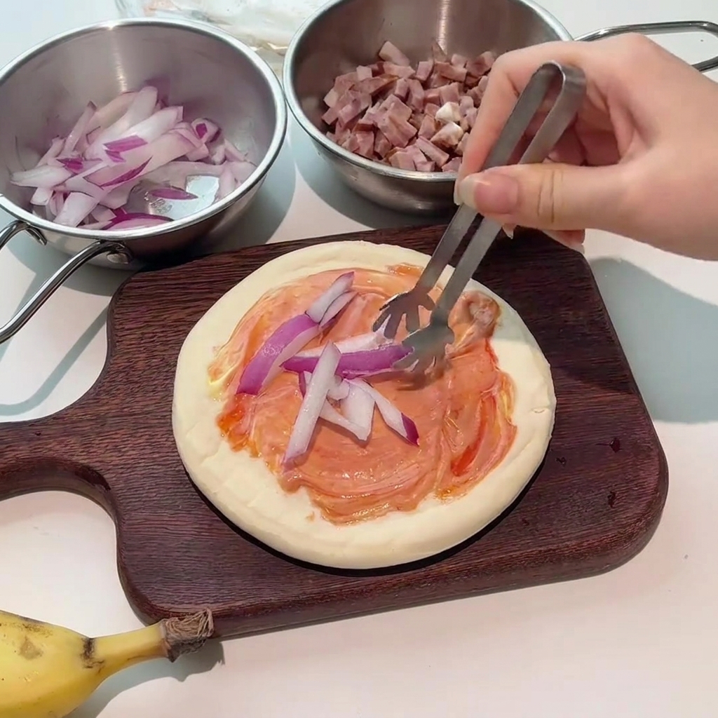 Pinzas colocando rodajas de cebolla roja fresca sobre la base con salsa.