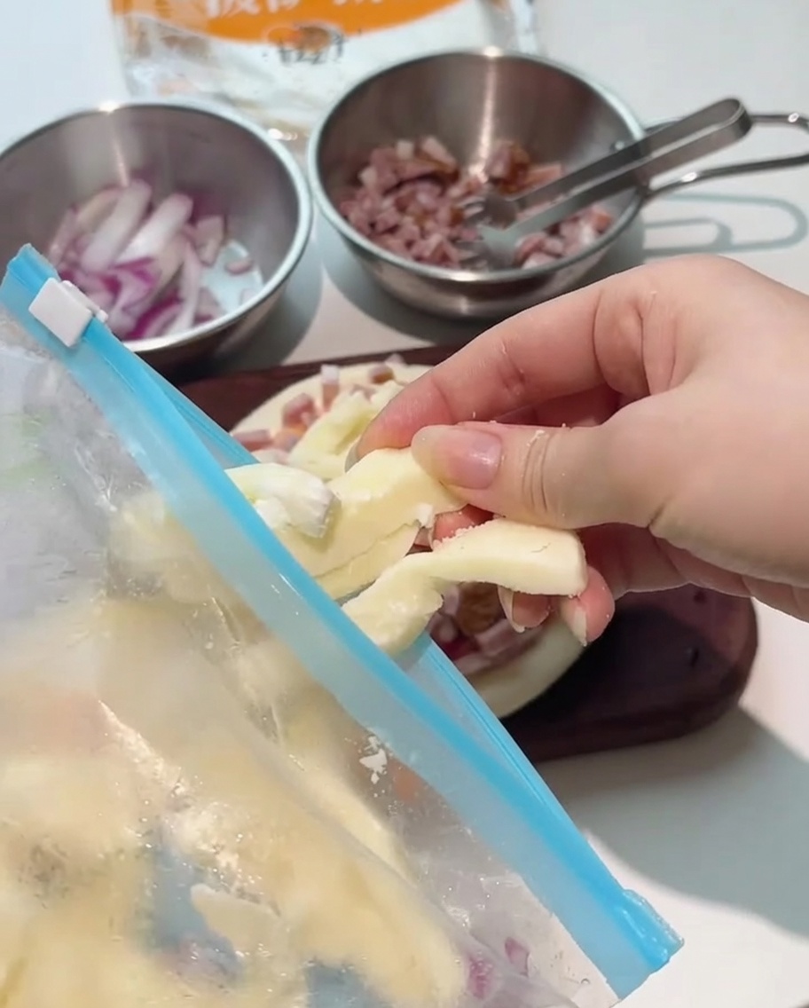 Tiras gruesas de queso mozzarella siendo colocadas sobre la pizza montada.