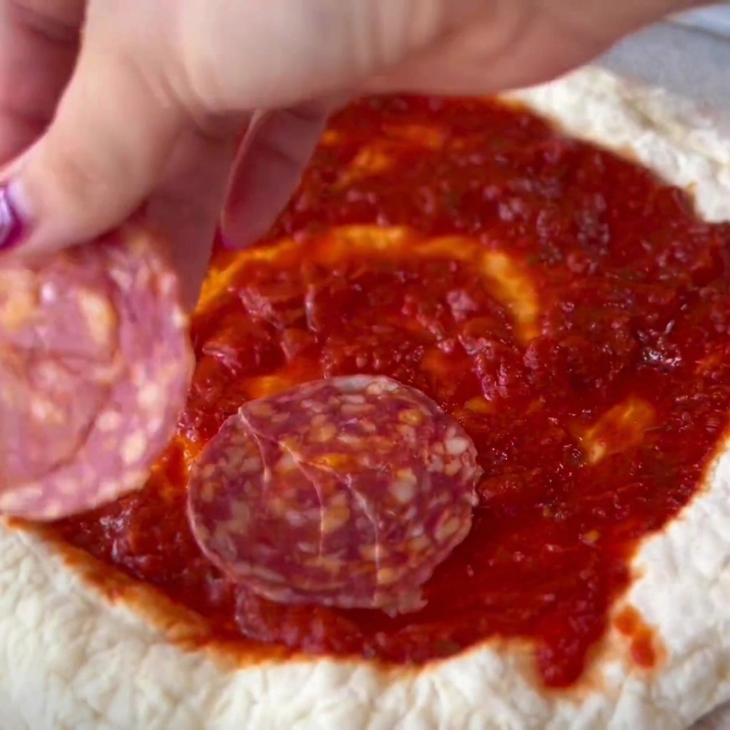 Rodajas de salami colocadas cuidadosamente sobre el centro con salsa de la masa de pizza.