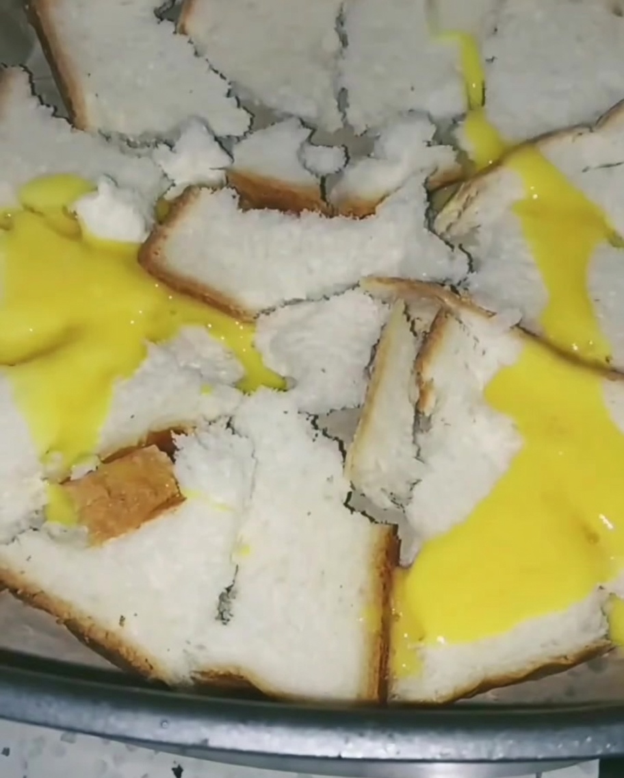 Huevos batidos siendo vertidos sobre el pan en la freidora, creando una capa amarilla fina sobre las piezas.