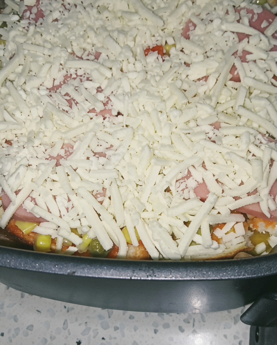 Primer plano de una capa generosa de queso rallado cubriendo el jamón y las verduras en la freidora.