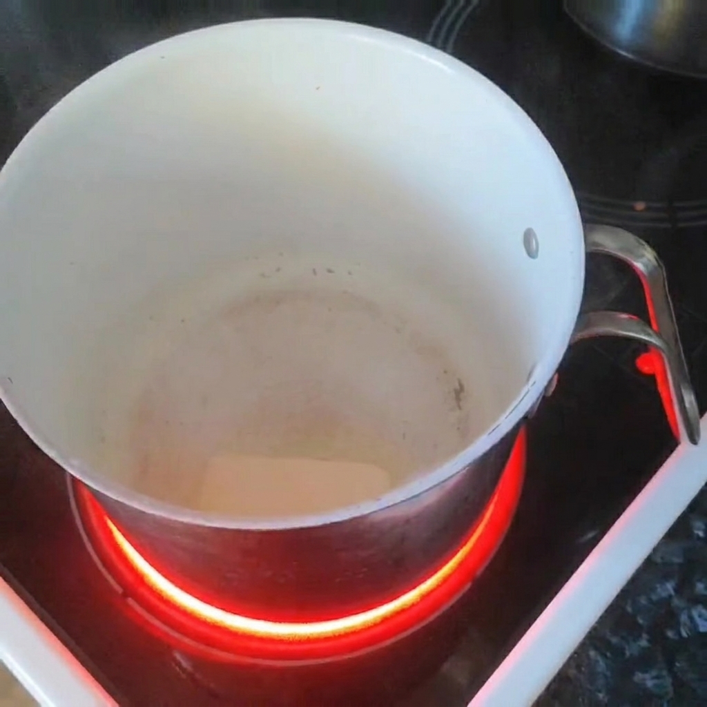 Un trozo de mantequilla derritiéndose en una cacerola blanca sobre una estufa de inducción.