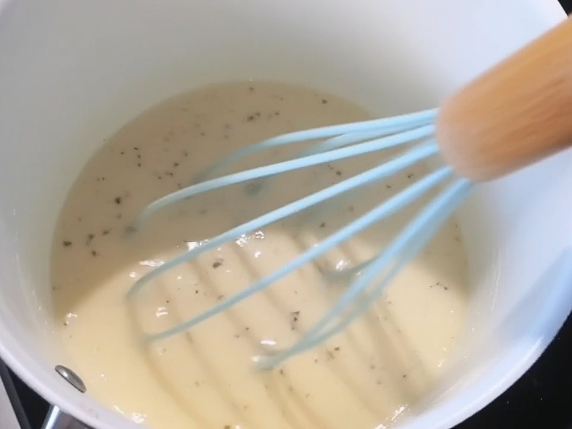 Sal, pimienta negra y queso rallado siendo añadidos a la salsa blanca cremosa.