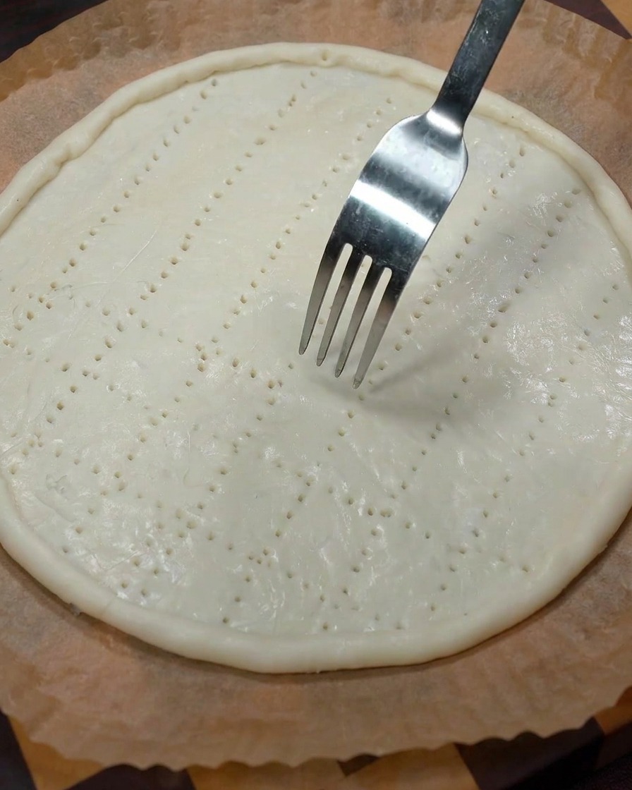 Un tenedor de metal perforando la base de la masa cruda para crear agujeros de ventilación.