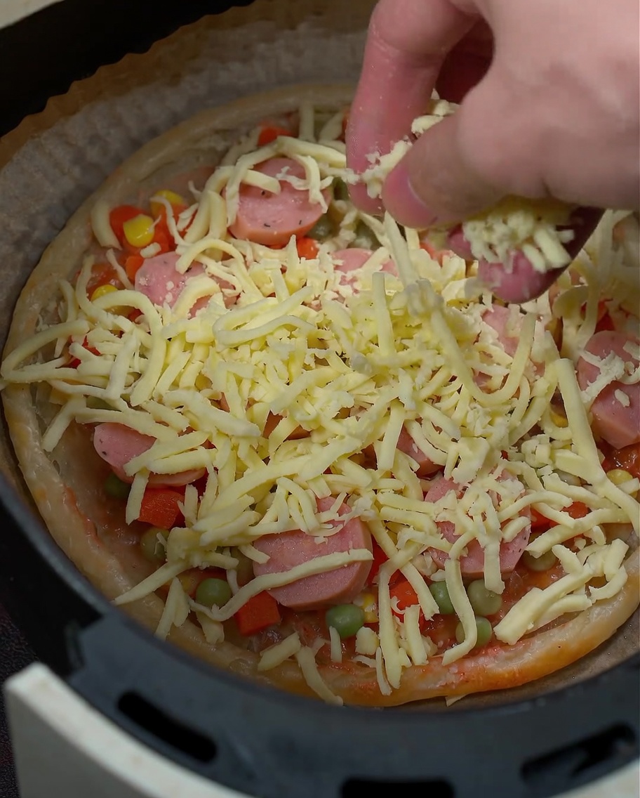 Primer plano de queso mozzarella espolvoreándose sobre los ingredientes de la pizza.