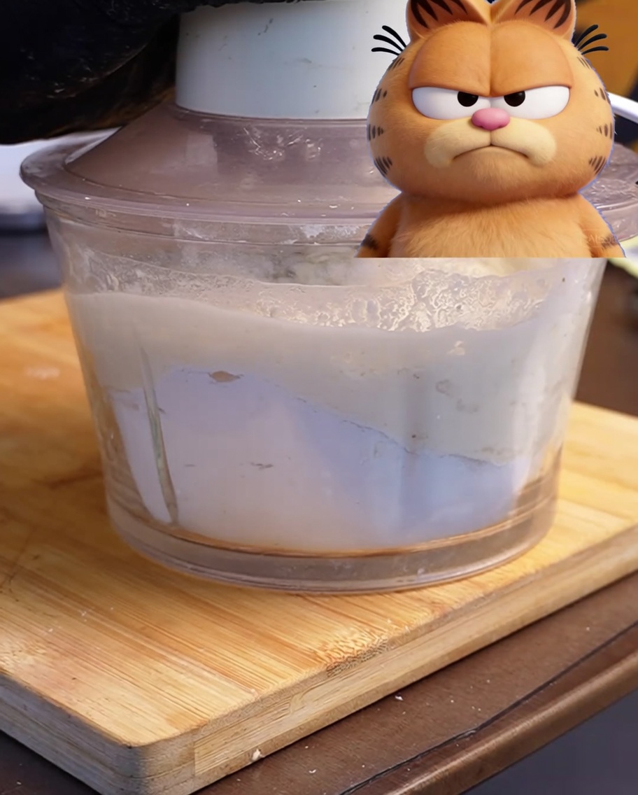 Un procesador de alimentos con los ingredientes para la masa de pizza sobre una tabla de madera.