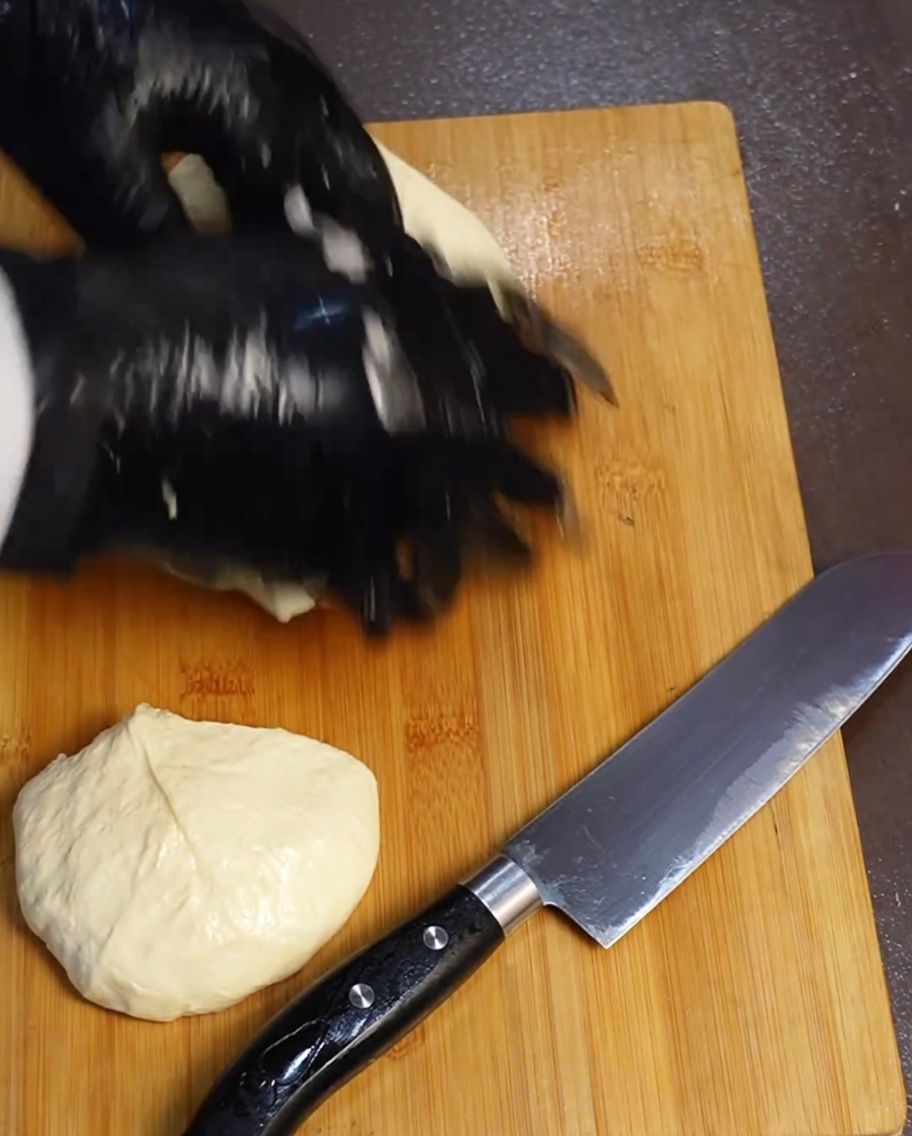 Cuatro porciones iguales de masa de pizza sobre una tabla de cortar de madera al lado de un cuchillo.