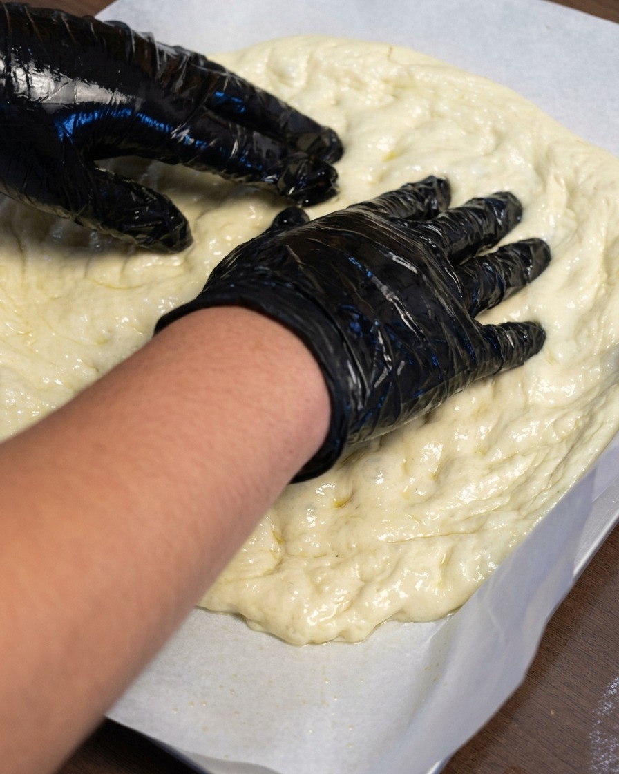 Manos estirando masa de pizza sobre una hoja de papel de horno.