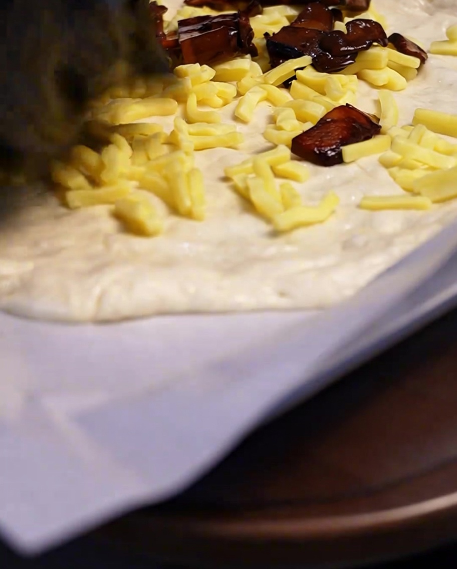 Champiñones fritos sazonados siendo colocados sobre una capa de queso en la base de la pizza.