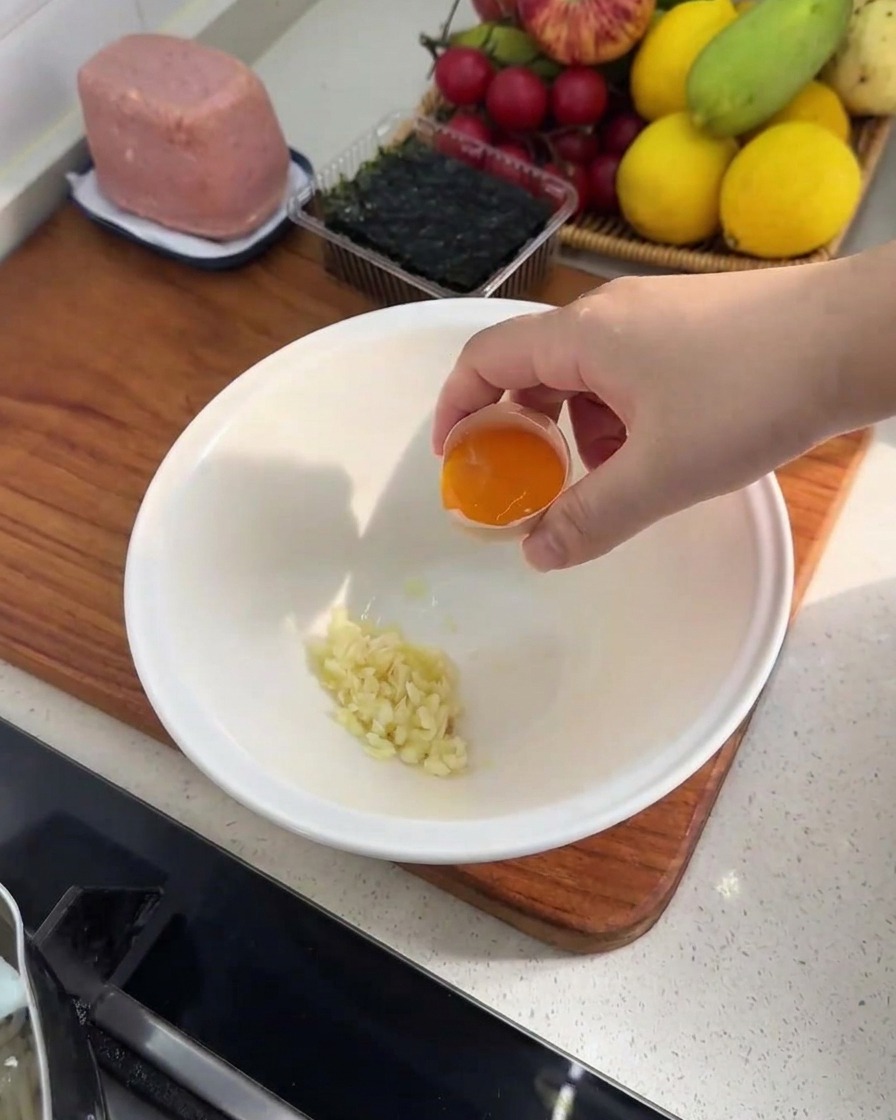Primer plano de un tazón blanco con ajo picado y una yema de huevo fresca.