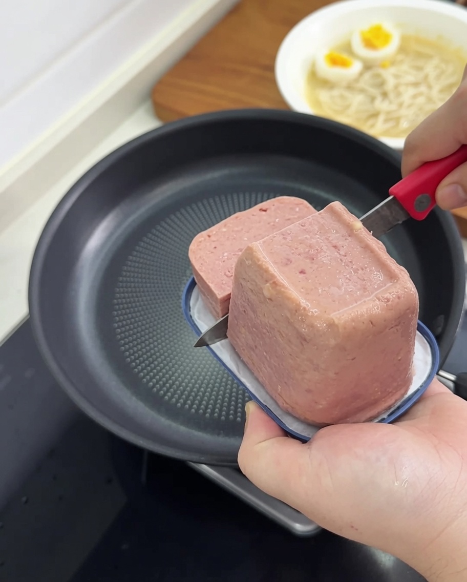 Rebanadas de carne de almuerzo friéndose en una sartén hasta dorar.