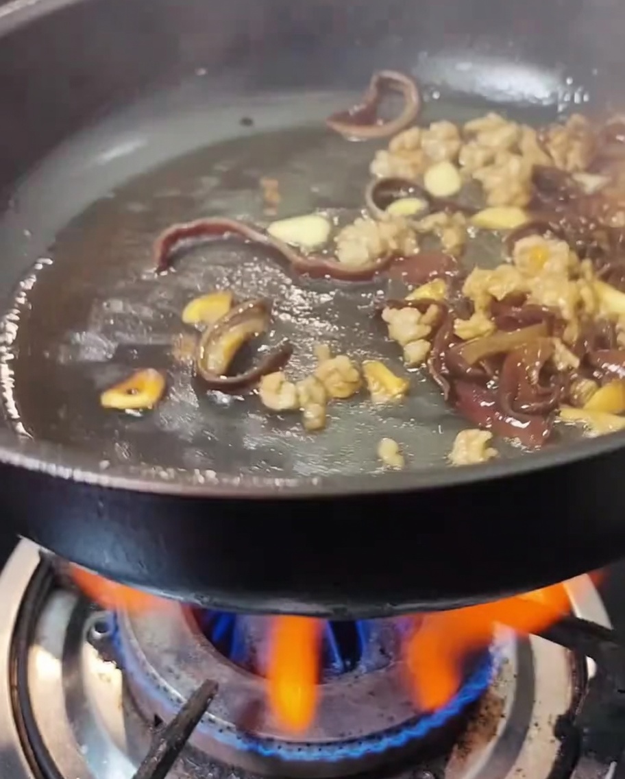 Salsa de soja y salsa de ostras siendo añadidas a la sartén con carne y hongos.
