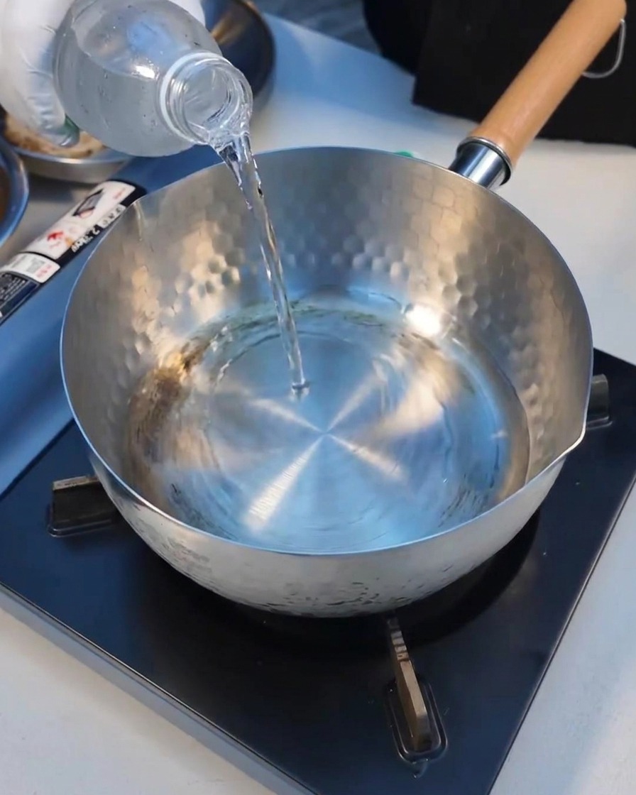 Agua mineral vertiéndose en una olla de metal limpia en la estufa.
