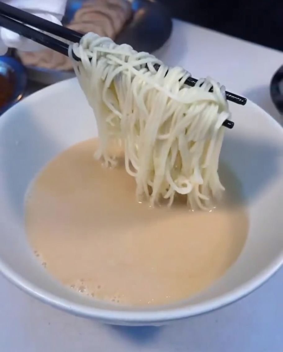 Fideos ramen humeantes transfiriéndose a un tazón de sopa.