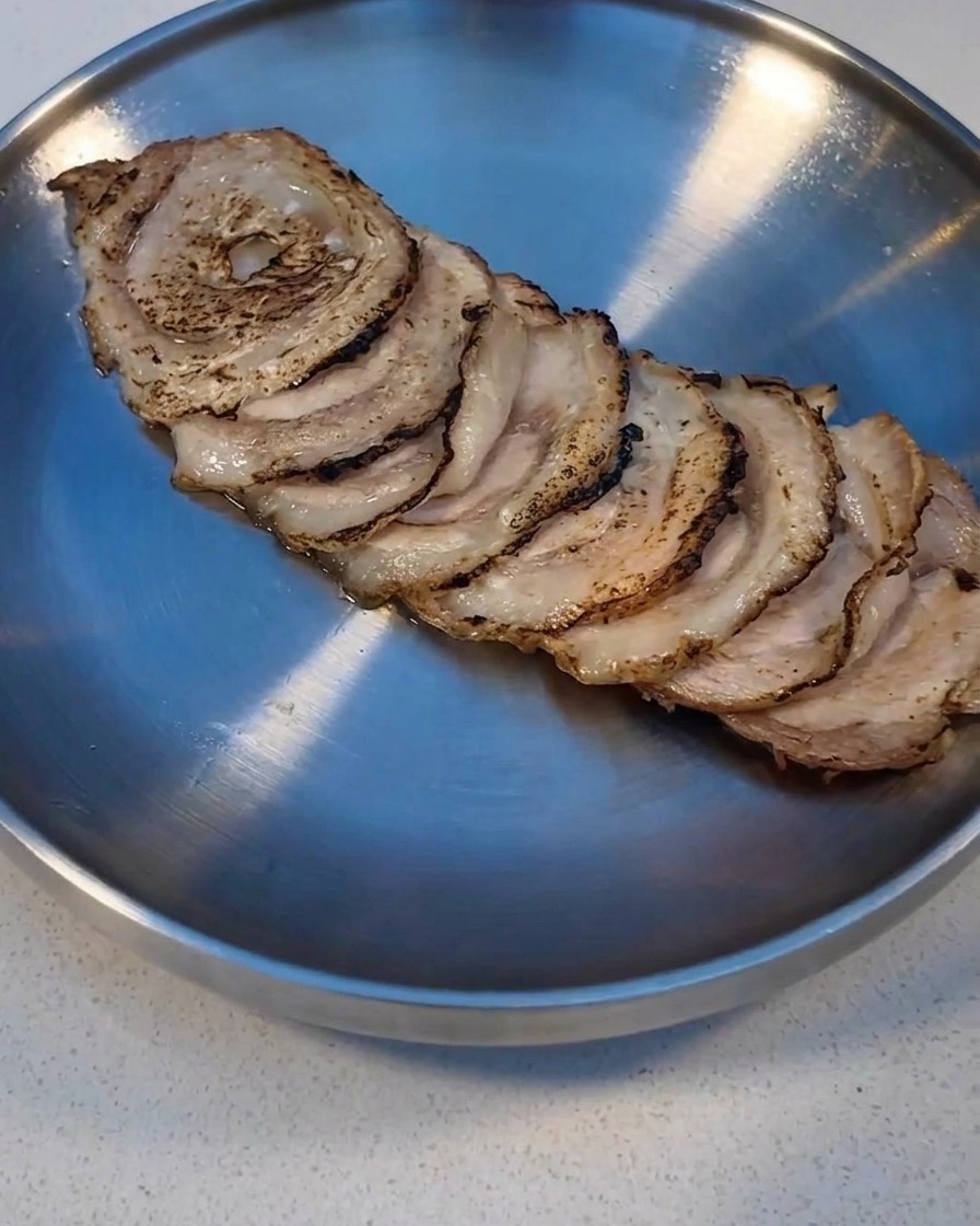 Rebanadas de Char Siu sellándose con un soplete de cocina en una bandeja de metal.