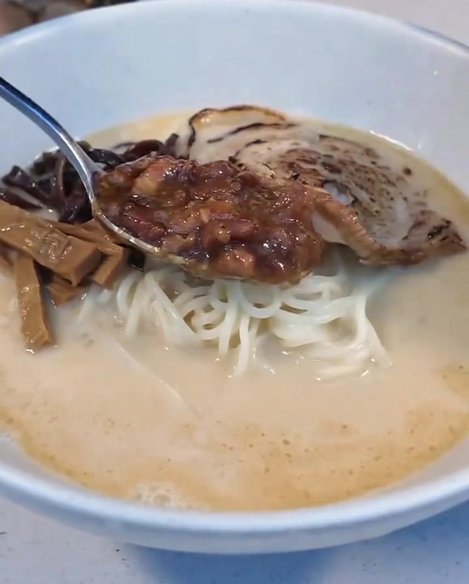 Una cucharada de salsa de carne estofada colocándose en el tazón de ramen junto a la mitad de un huevo pasado por agua.
