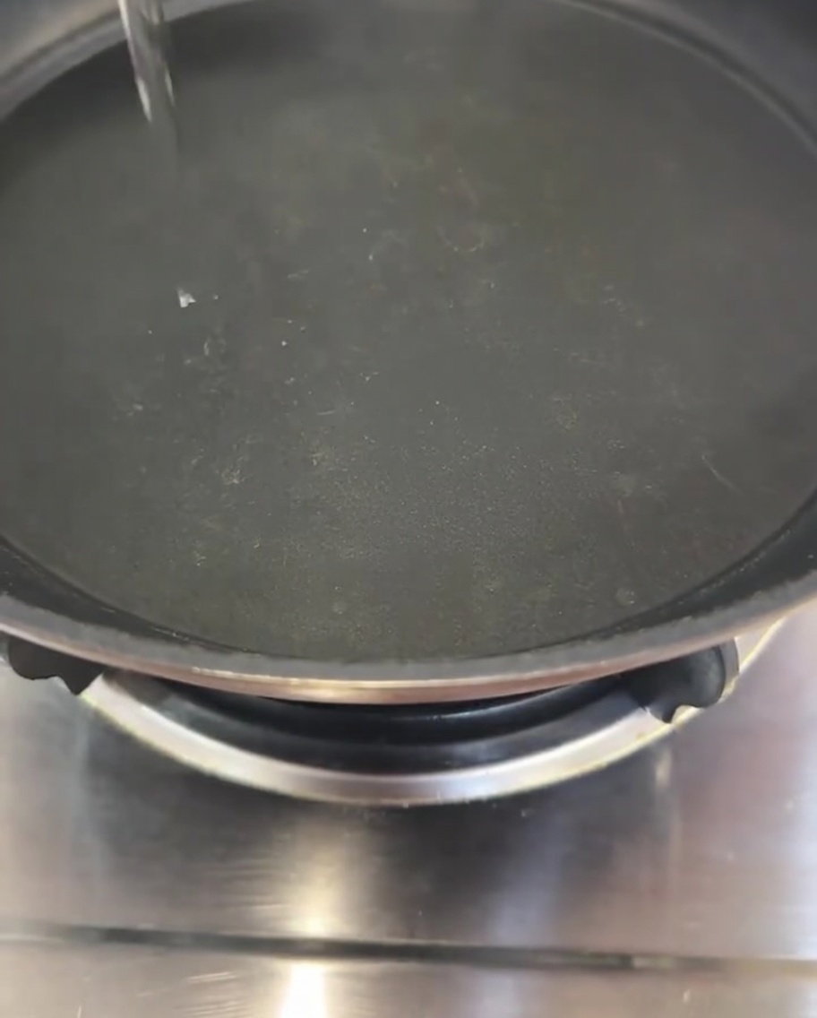 Un chorrito de aceite cayendo en el centro de una sartén negra.