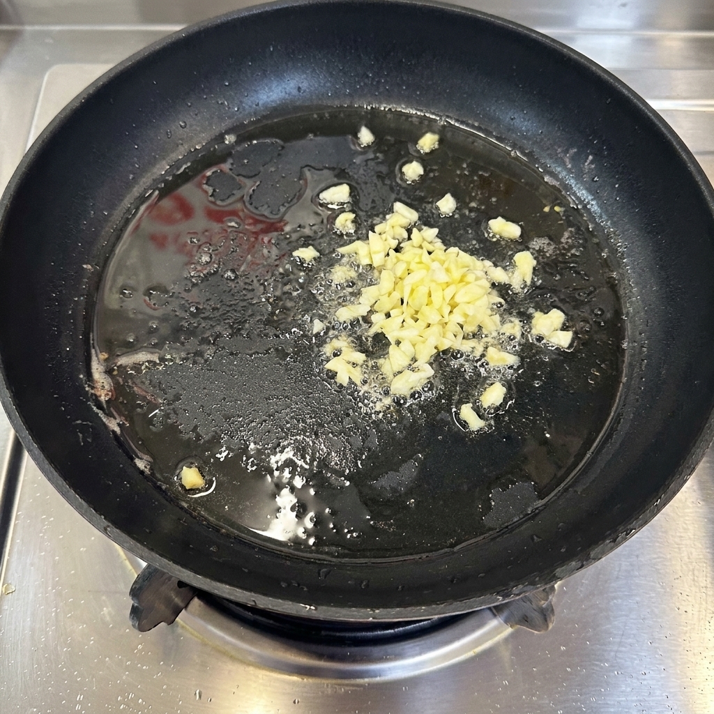 Ajo picado dorándose en aceite dentro de una sartén negra.