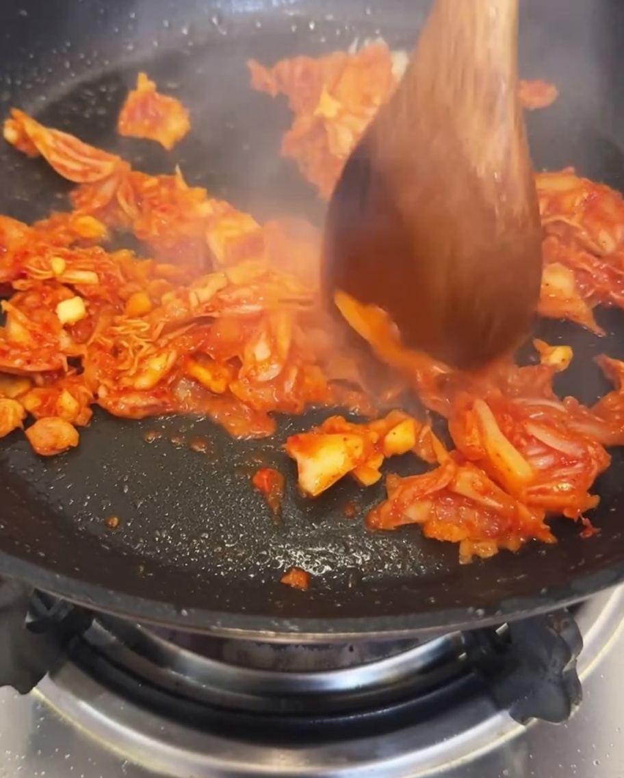 Agua siendo vertida en la sartén con el kimchi y el ajo.