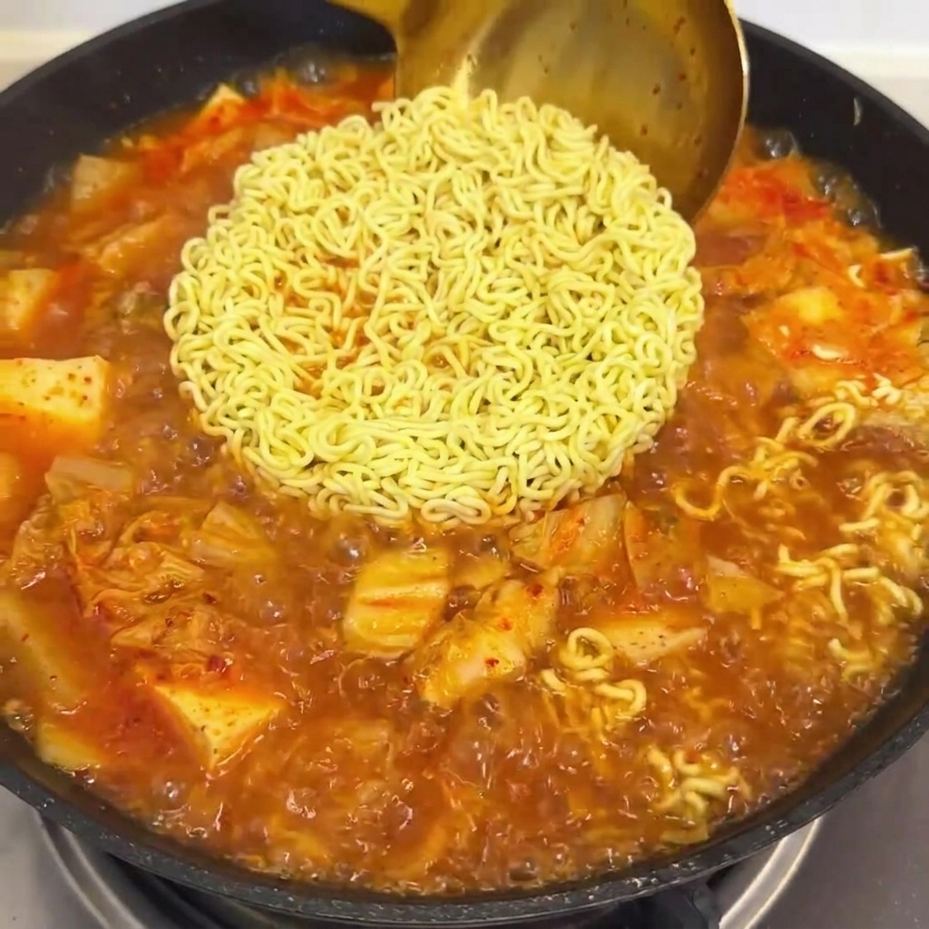 Salsa roja vertida en la sartén con los fideos y el caldo.