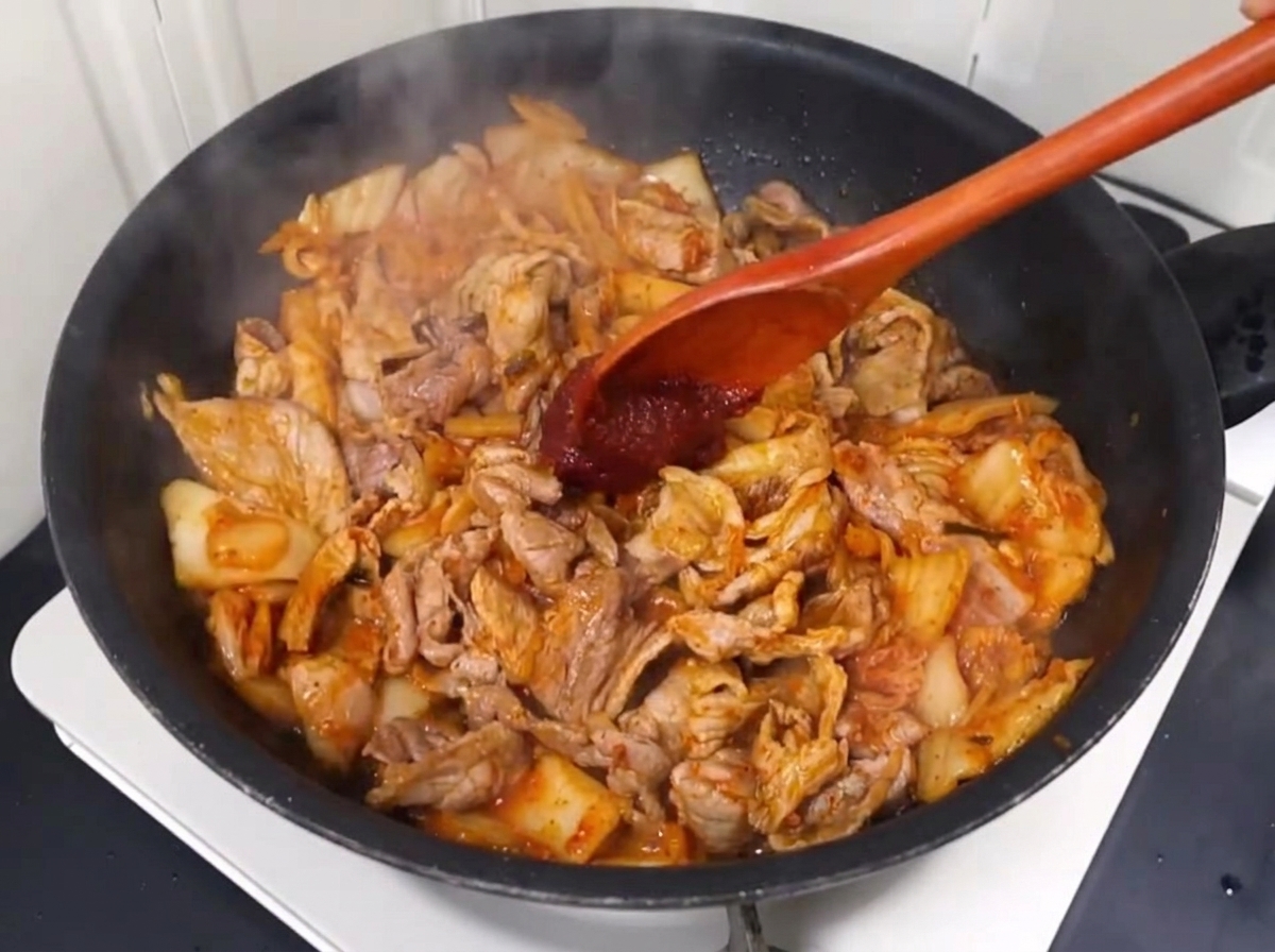 Pasta de chile y chile en polvo mezclándose en el salteado de cerdo y kimchi.
