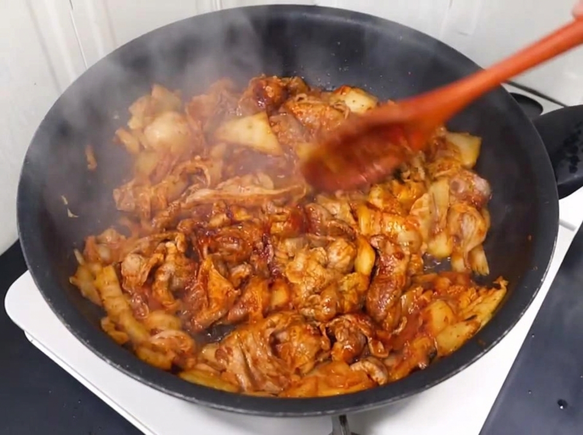 Agua vertiéndose en la sartén con el salteado de cerdo y kimchi.