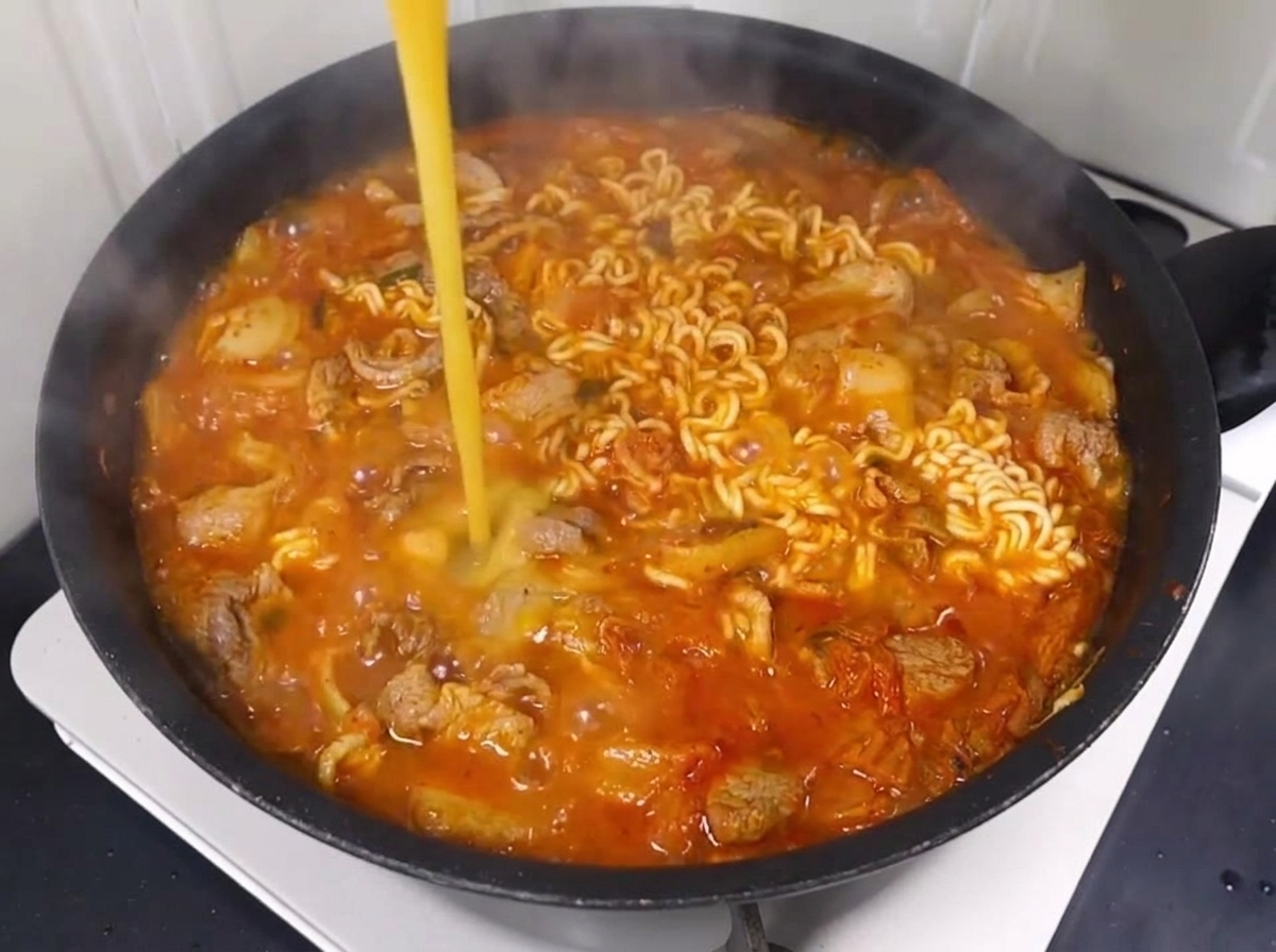 Un huevo batido removiéndose en el burbujeante caldo de ramen con fideos, cerdo y kimchi.