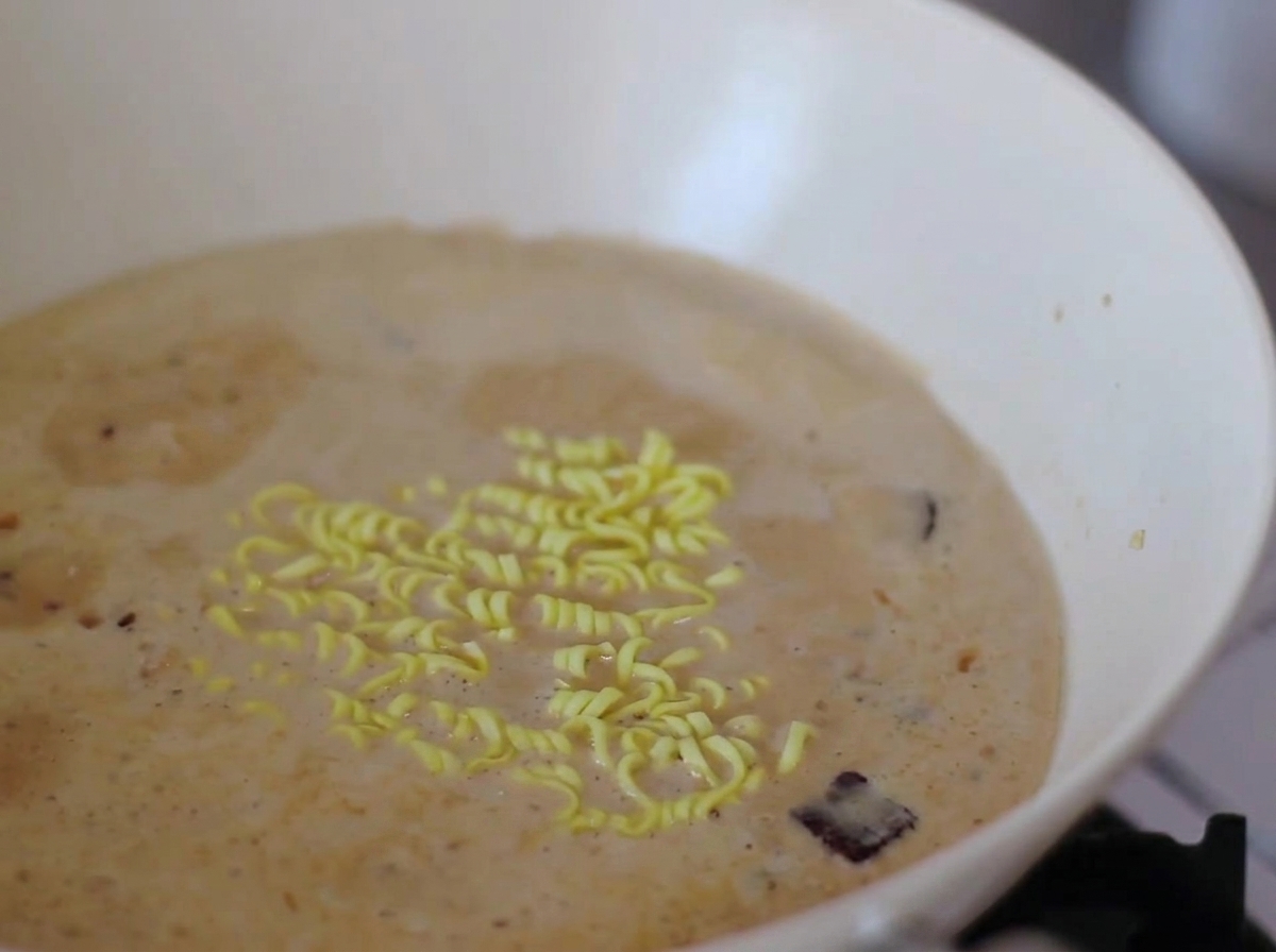 Fideos instantáneos y rodajas de pastel de pescado narutomaki hirviendo en un caldo cremoso.