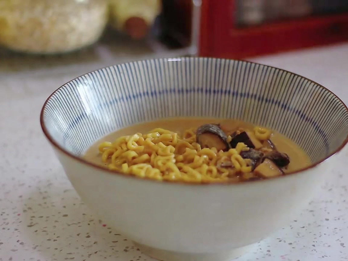 Fideos de ramen y caldo cremoso siendo servidos con un cazo en un tazón a rayas.