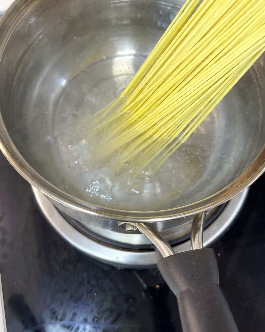 Fideos sumergidos en una olla con agua hirviendo, removidos con palillos.