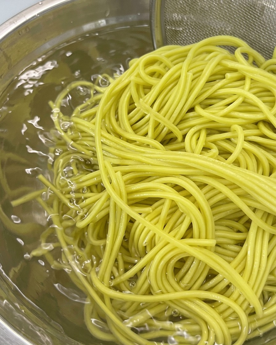 Un colador con fideos hervidos sumergiéndose en un bol de agua fría para enjuagarlos.