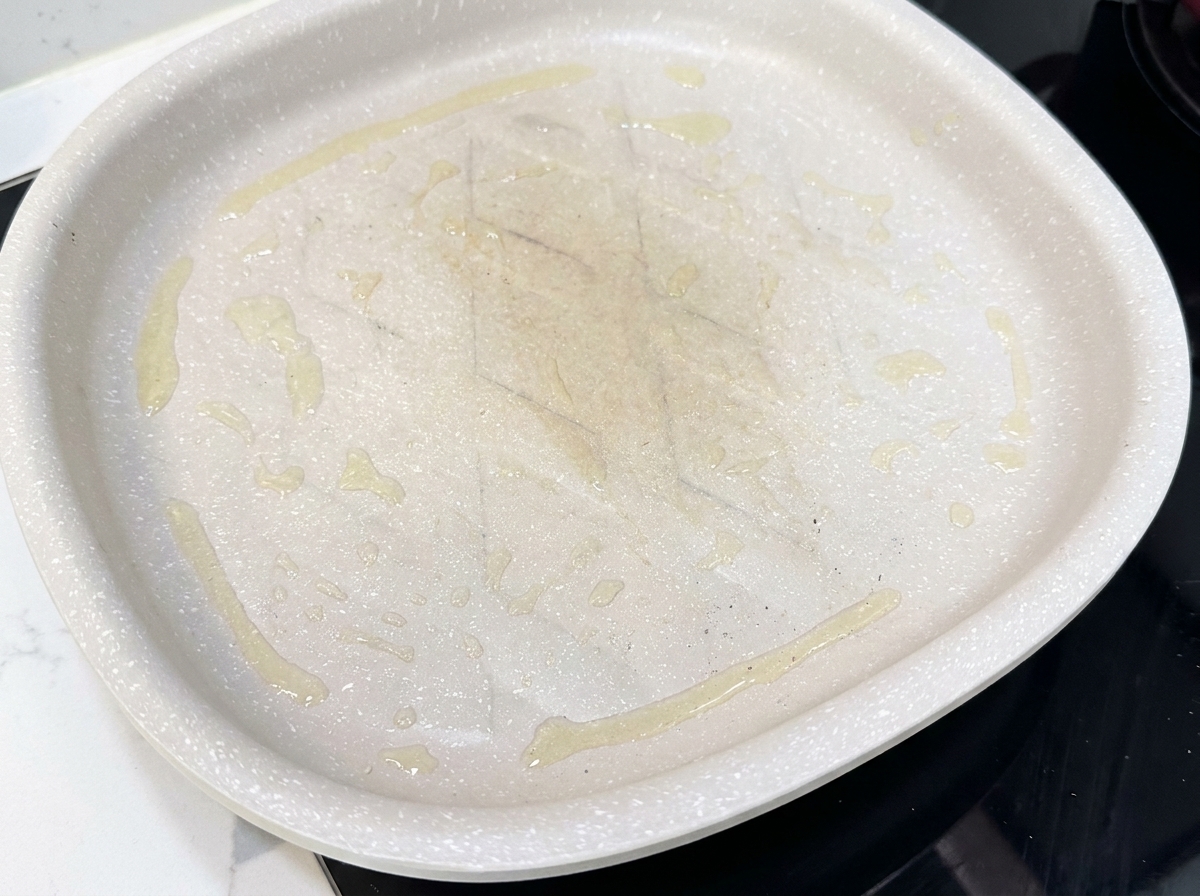 Tiras de tocino extendidas en una sartén antiadherente caliente, empezando a cocinarse.