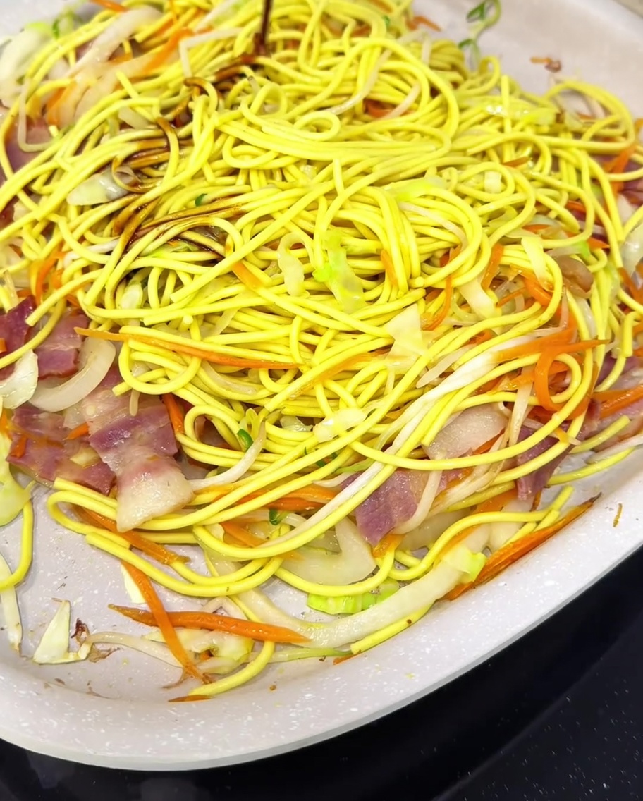 Fideos y verduras salteándose en una sartén con una mezcla de salsa inglesa, salsa de ostras, sake y azúcar.