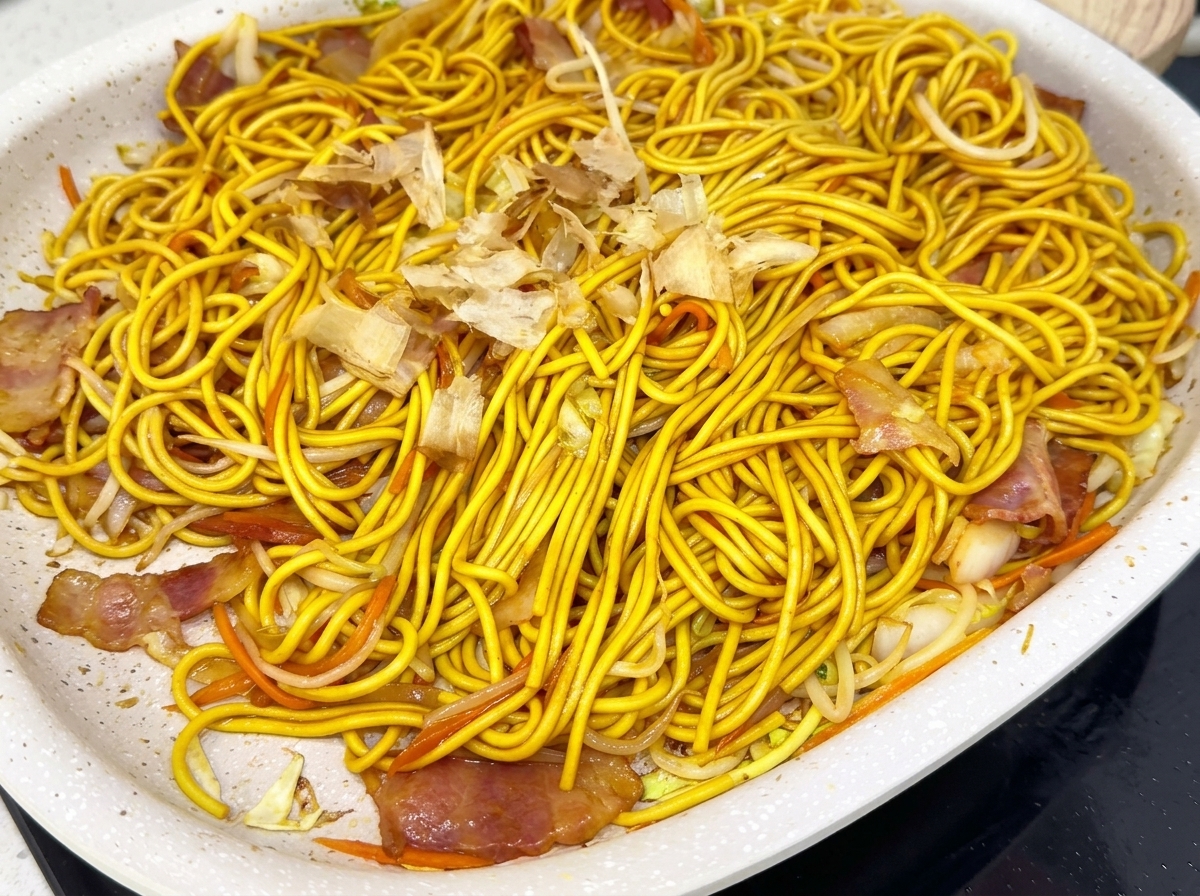 Una sartén llena de fideos fritos coronados con una capa de copos de bonito.