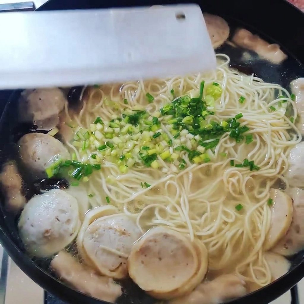 Vista desde arriba de una olla con fideos, albóndigas y otros ingredientes decorados con cebolleta picada.