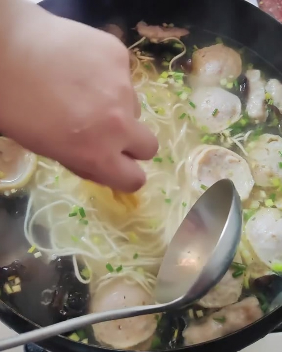Una mano colocando rodajas finas de limón amarillo en una olla de fideos y caldo cocidos.