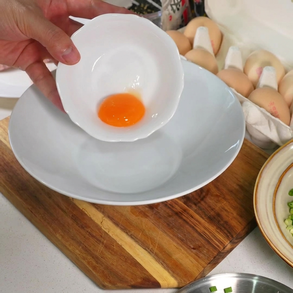 Una yema de huevo cruda y vibrante en el fondo de un tazón de cerámica blanca.