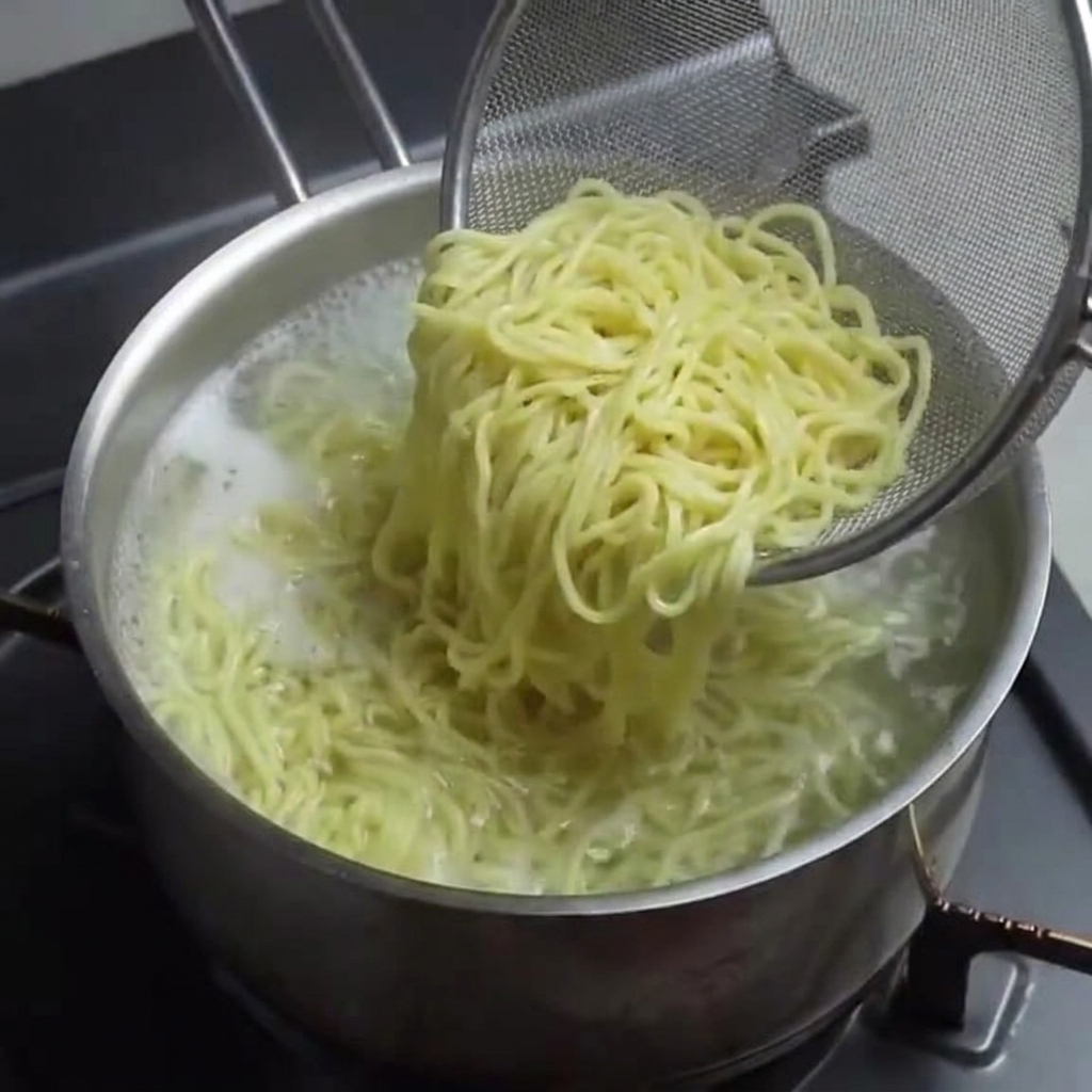 Fideos de ramen cocidos siendo retirados de una olla con un colador de malla de alambre.