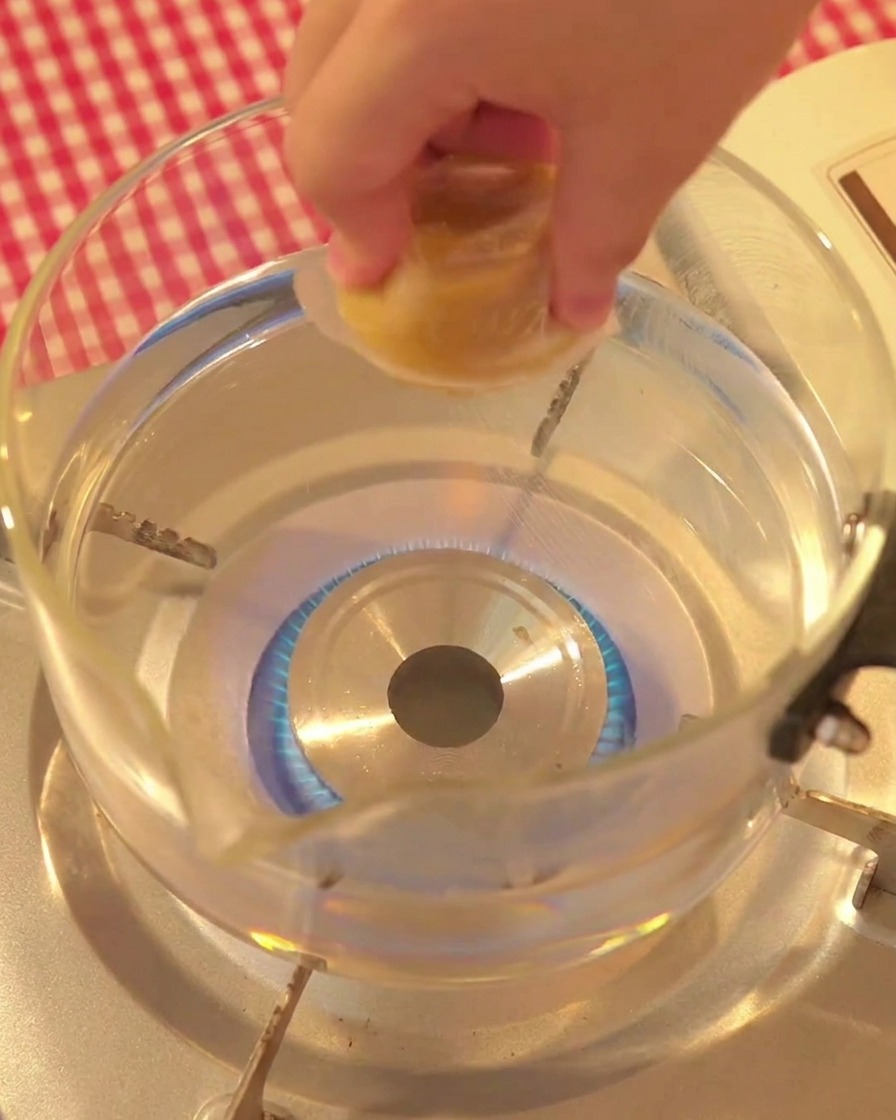 Mano colocando un cubo de caldo de pollo en una olla de vidrio con agua hirviendo.
