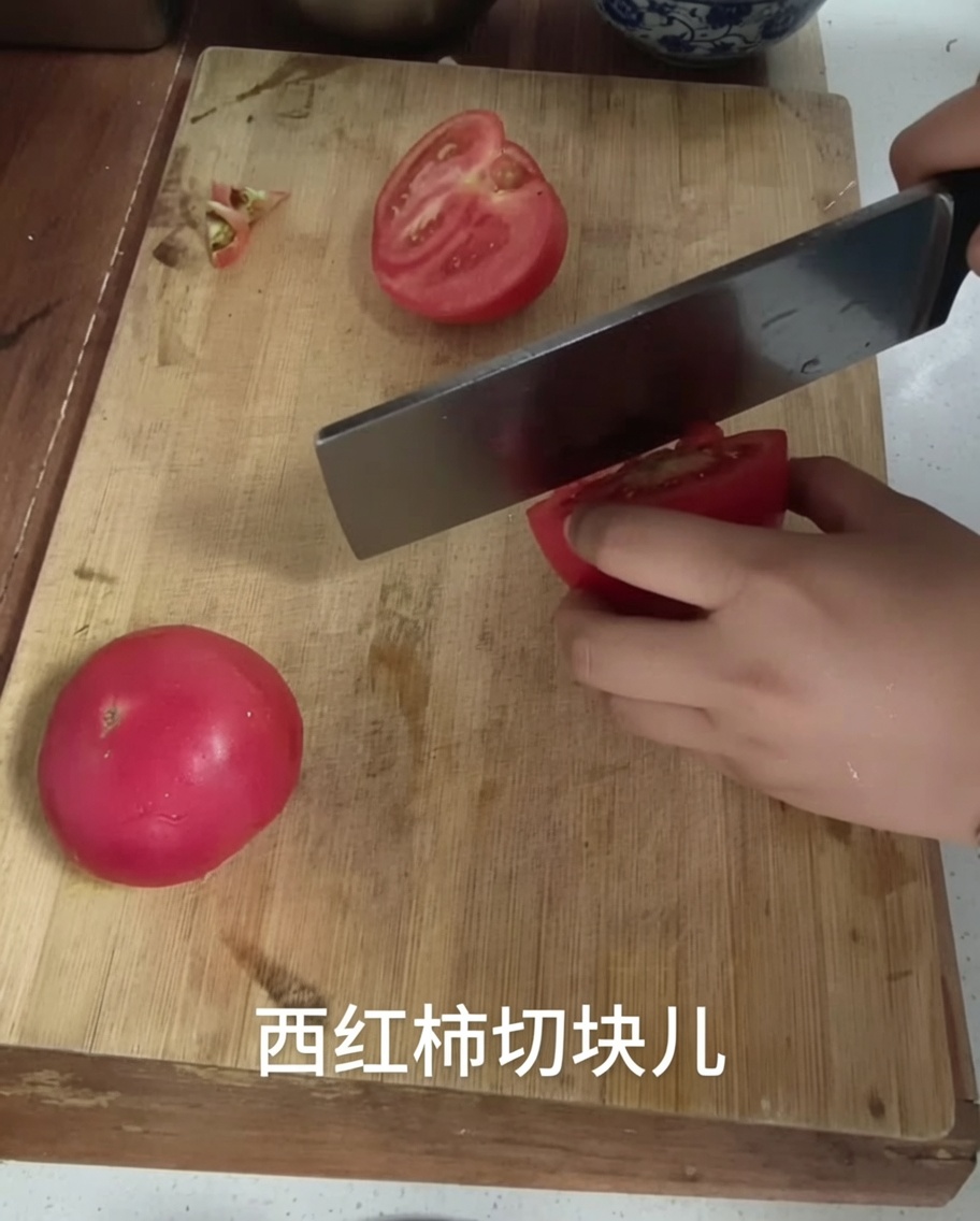 Cuchillo cortando un tomate en trozos sobre una tabla de madera.