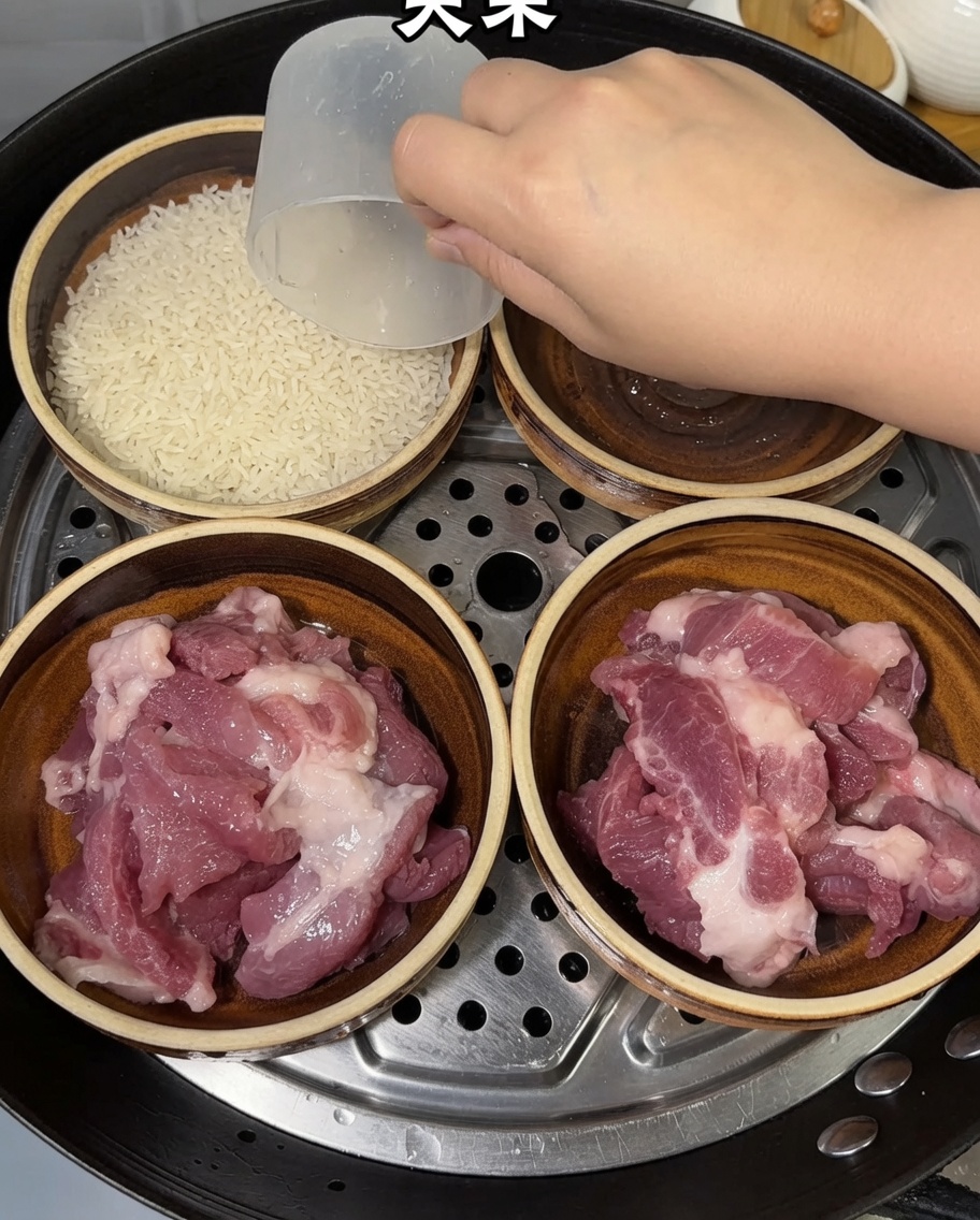 Una mano usando una taza medidora para añadir arroz crudo en cuencos que ya contienen trozos de cerdo.